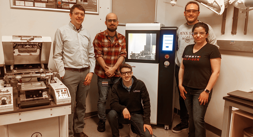 group of people standing around a 3D printer in a lab