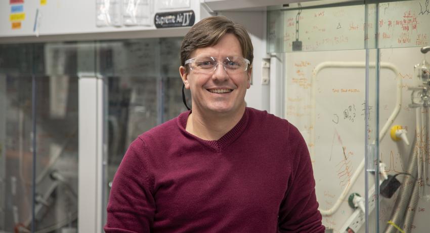 Man in safety glasses standing in front of a large piece of lab equipment